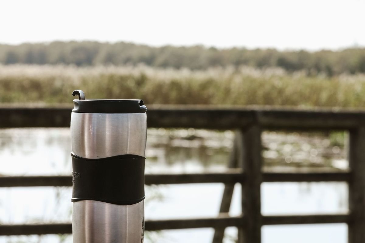 Stainless steel travel mug on a wooden table by a lake (representative photo, not the exact product)