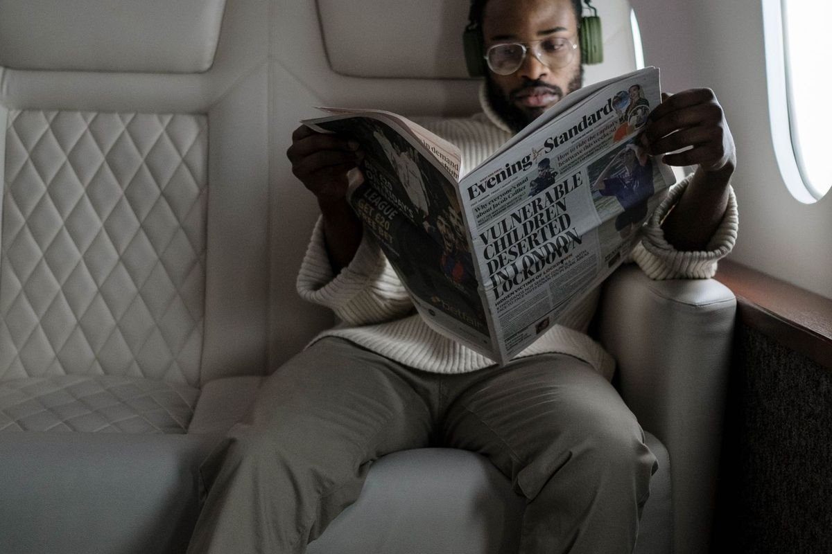 Man wearing over-ear headphones reading a newspaper on a plane (representative photo, not the exact product)