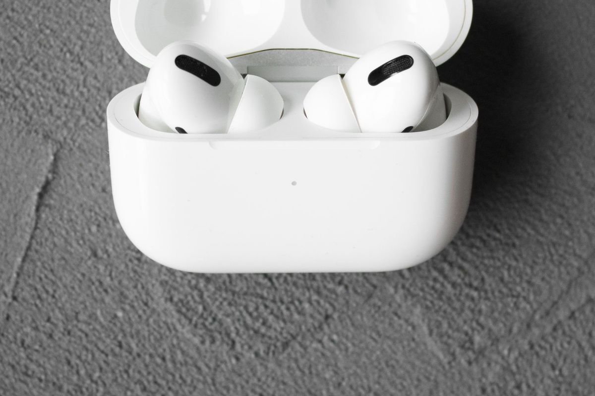 White wireless earbuds in an open charging case on a textured gray surface (representative photo, not the exact product)