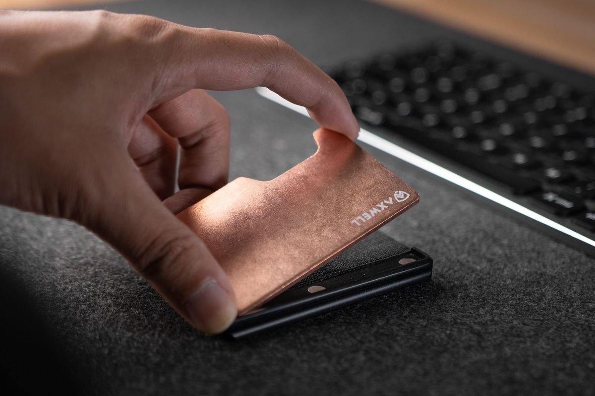 Hand holding a slim metal wallet above a desk with a keyboard (representative photo, not the exact product)