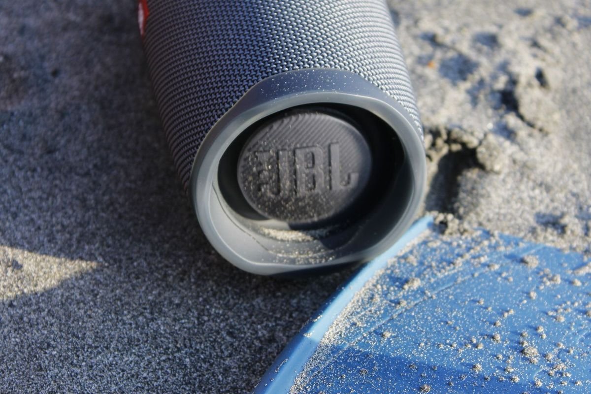 Gray portable Bluetooth speaker lying on a sandy beach (representative photo, not the exact product)