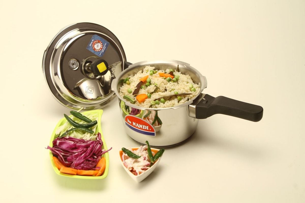 Stainless steel pressure cooker next to bowls of rice and vegetables (representative photo, not the exact product)