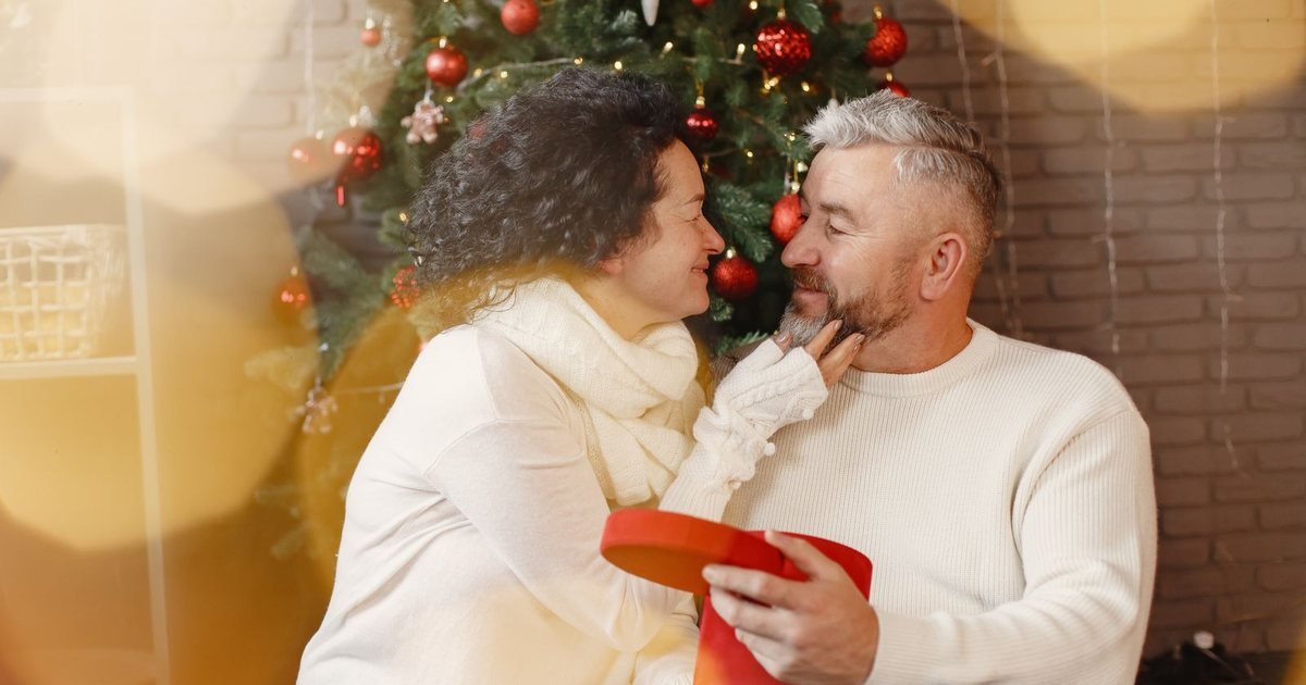 Happy older couple exchanging a gift by the Christmas tree