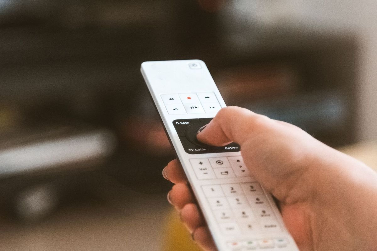 Hand holding a TV remote in a cozy living room (representative photo, not the exact product)
