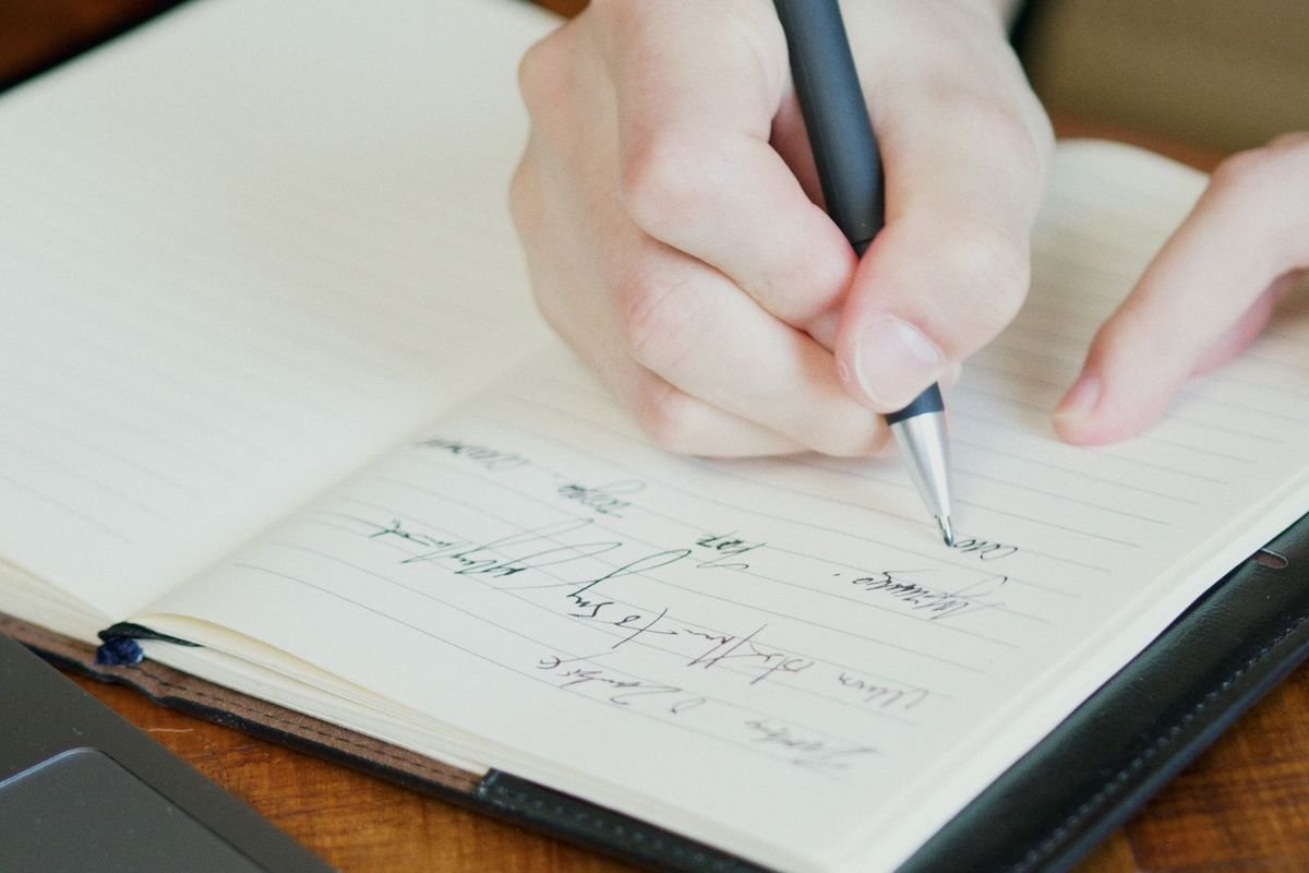 Person writing in a notebook with a pen (representative photo, not the exact product)