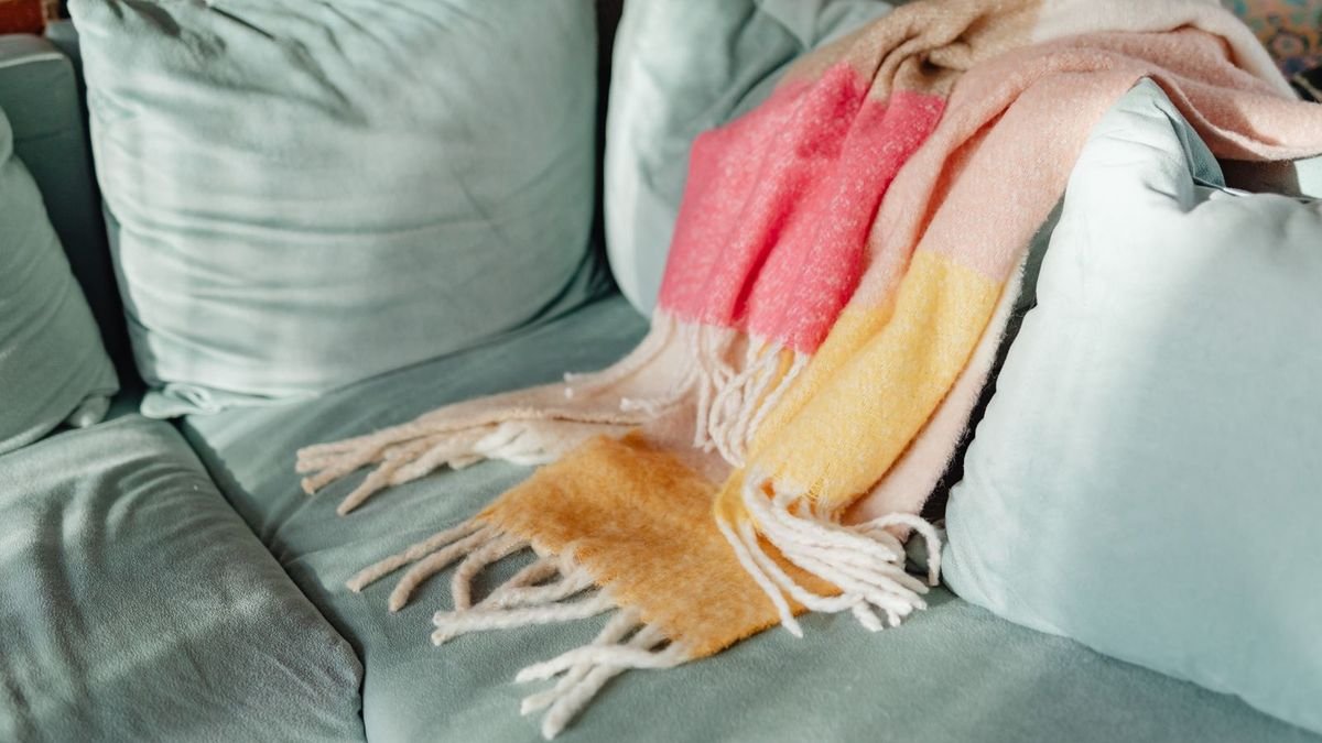 Colorful knit throw blanket draped over a teal sofa (representative photo, not a heated blanket)