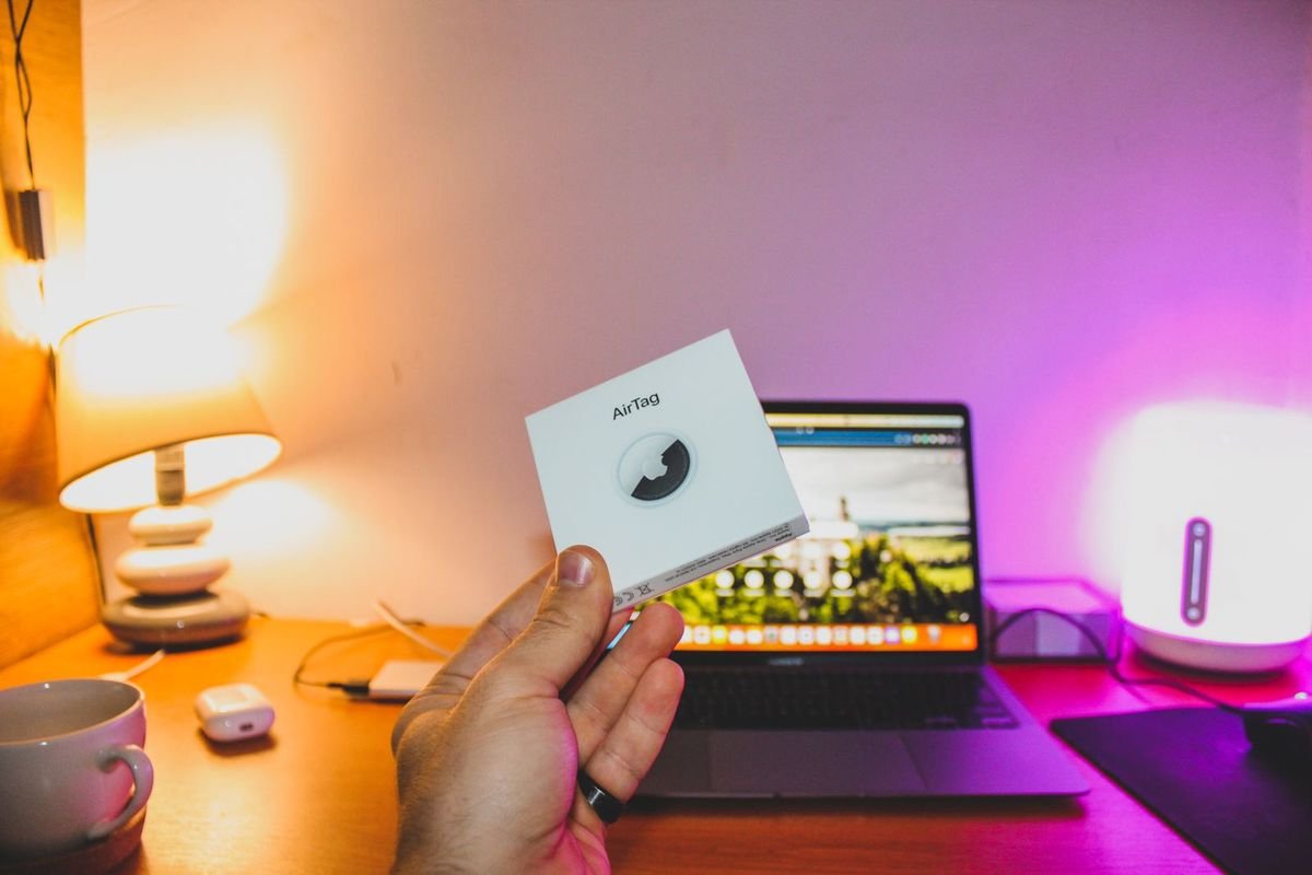 Hand holding an item tracker box in front of a laptop (representative photo, not the exact product)