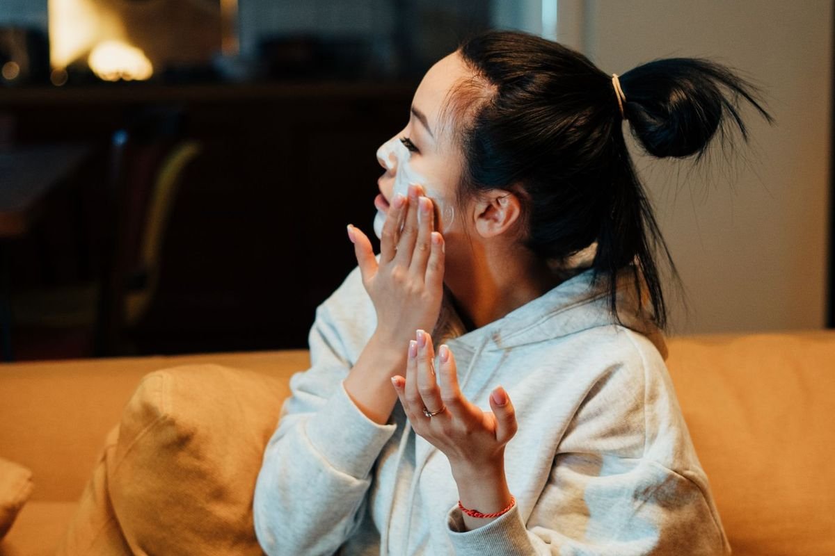 Woman in a cozy sweatshirt relaxing on a couch with a face mask