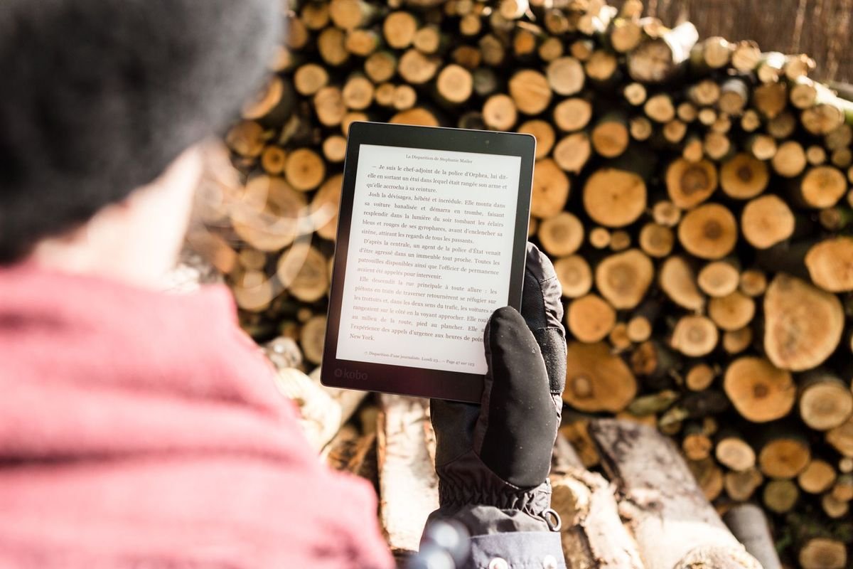 Person holding an e-reader near firewood (representative photo, not the exact product)