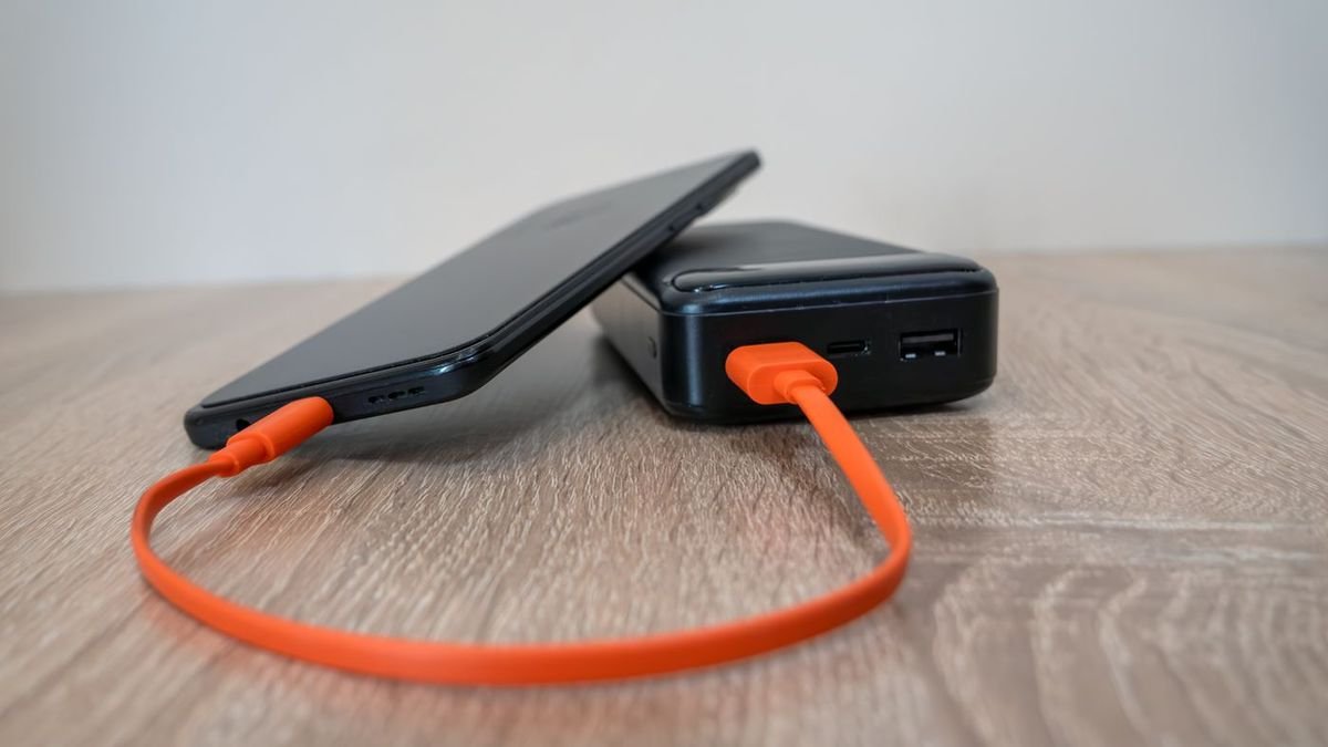 Smartphone charging from a portable power bank with an orange cable on a wooden table