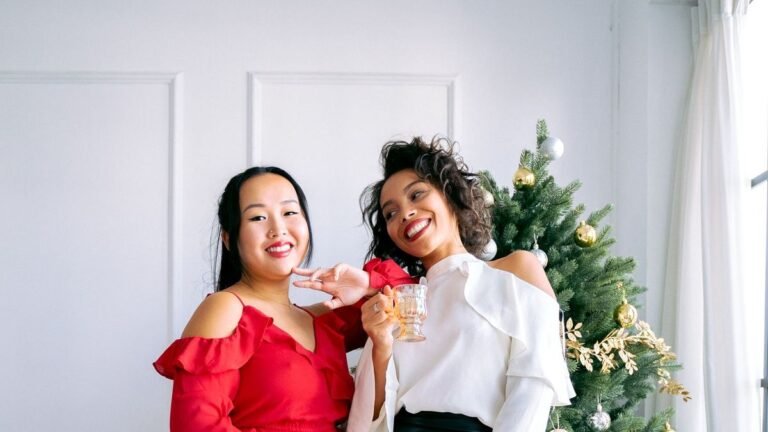 Two smiling women posing together next to a decorated Christmas tree with gifts
