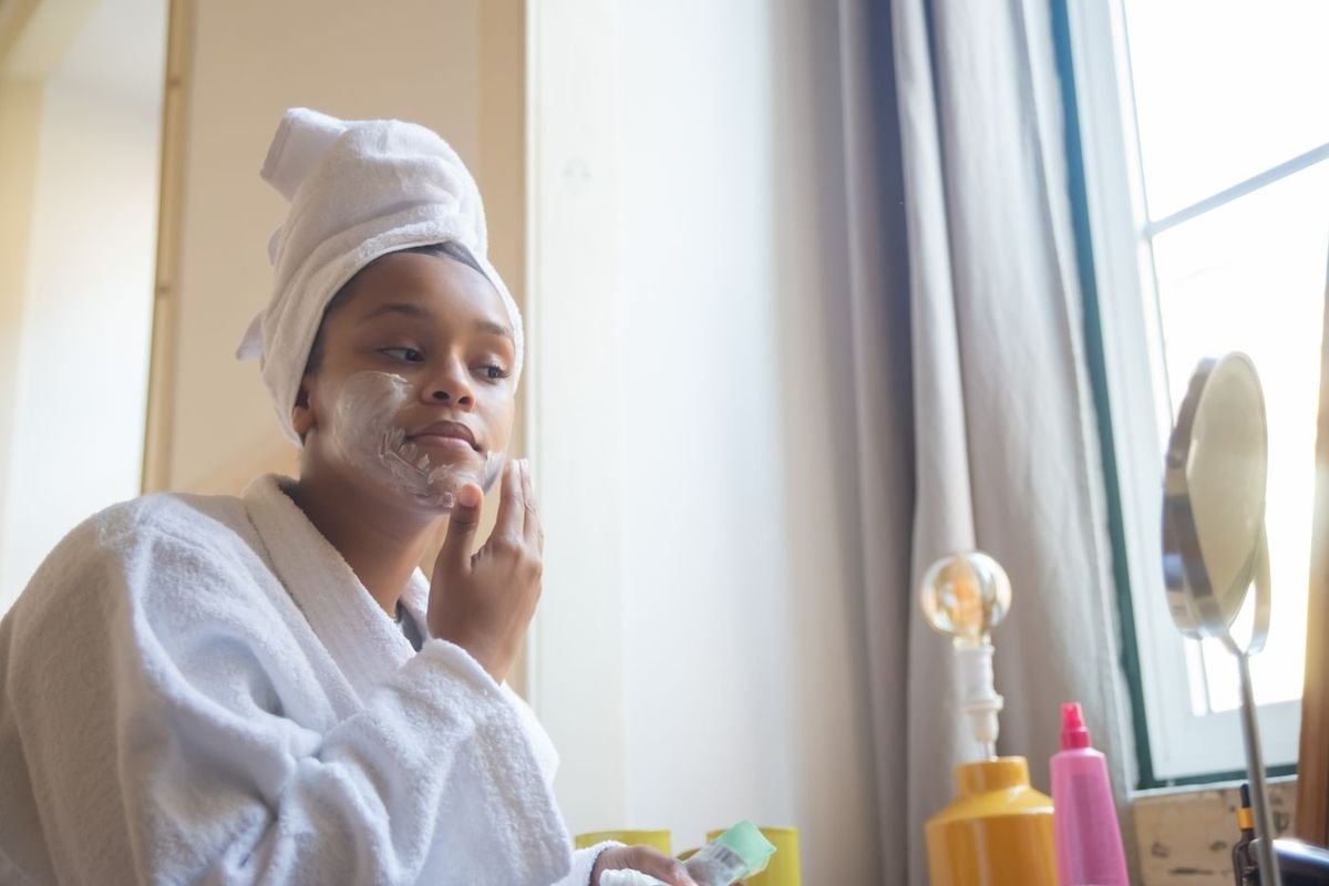 Woman in a white bathrobe and hair towel applying a face mask during an at-home spa moment