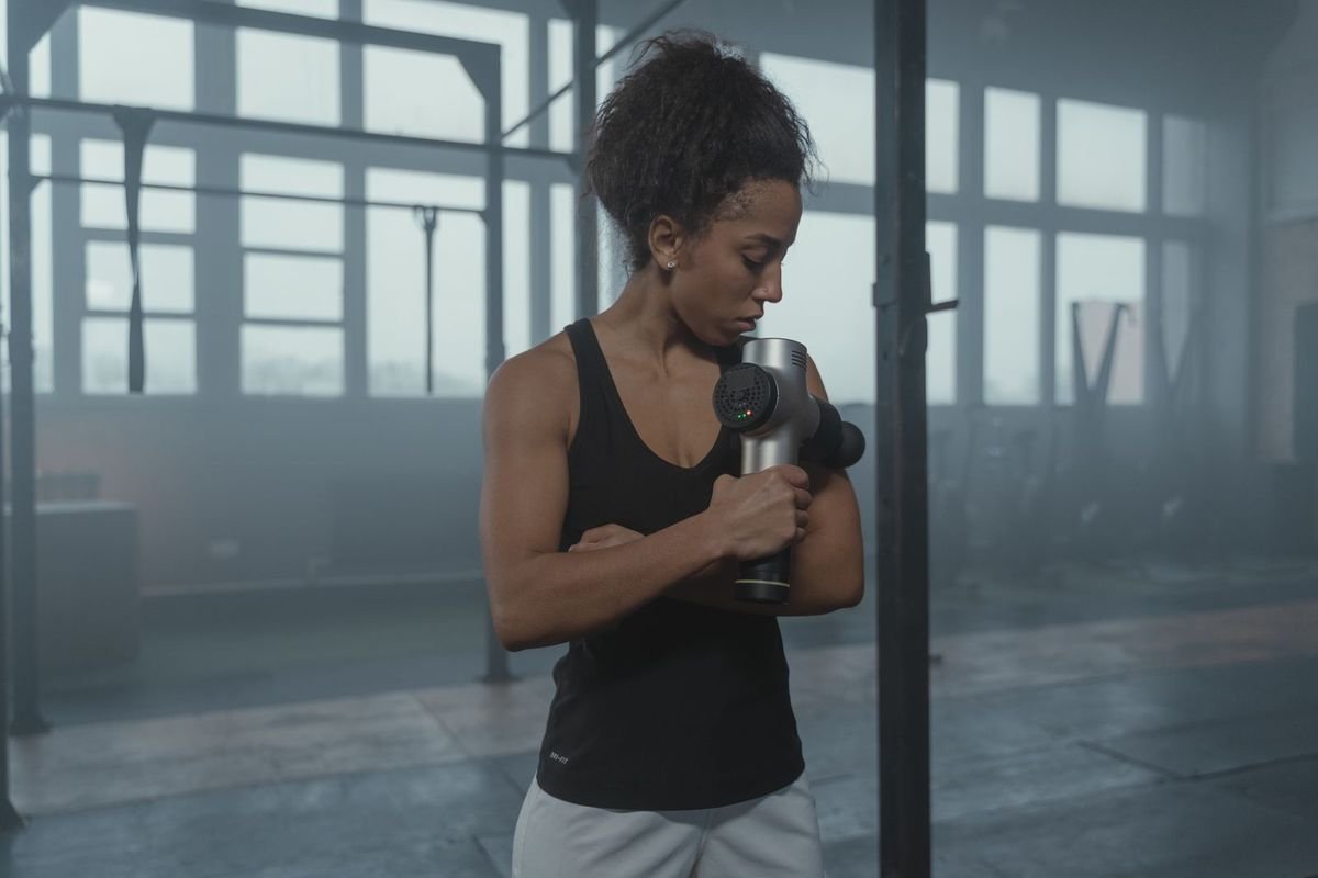 Woman using a massage gun in a gym (representative photo, not the exact product)