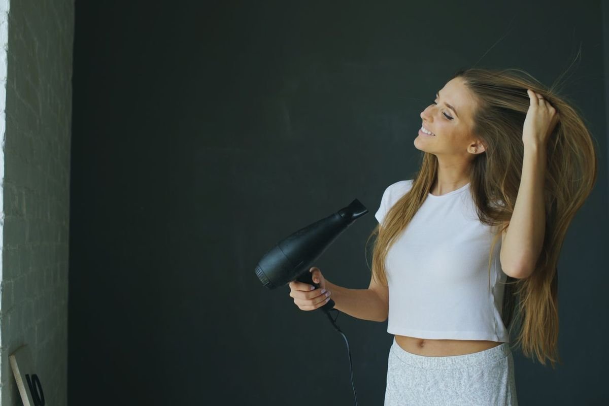 Woman drying long hair with a hair dryer indoors (representative photo, not the exact product)