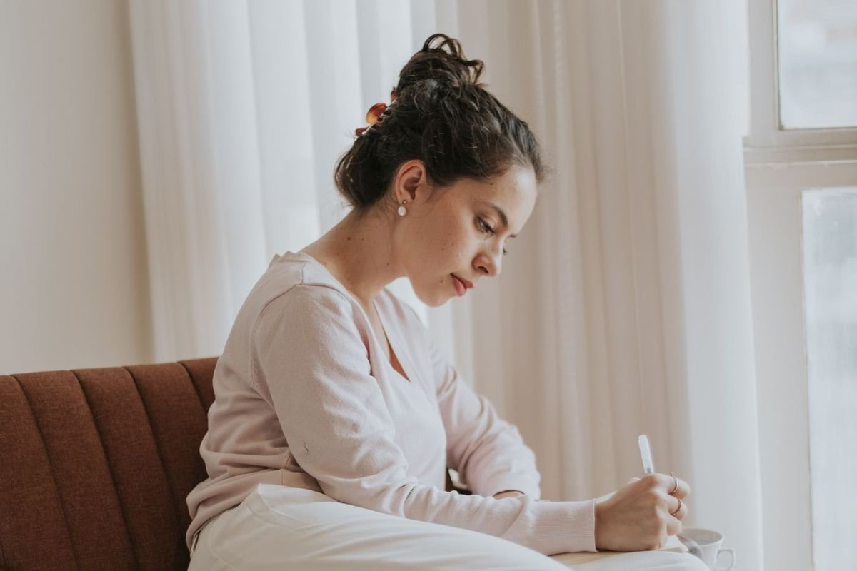 Woman journaling in a cozy armchair next to a sunny window