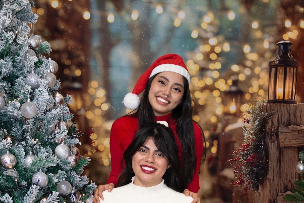 Two smiling women in Christmas outfits posing together in front of a glowing Christmas tree