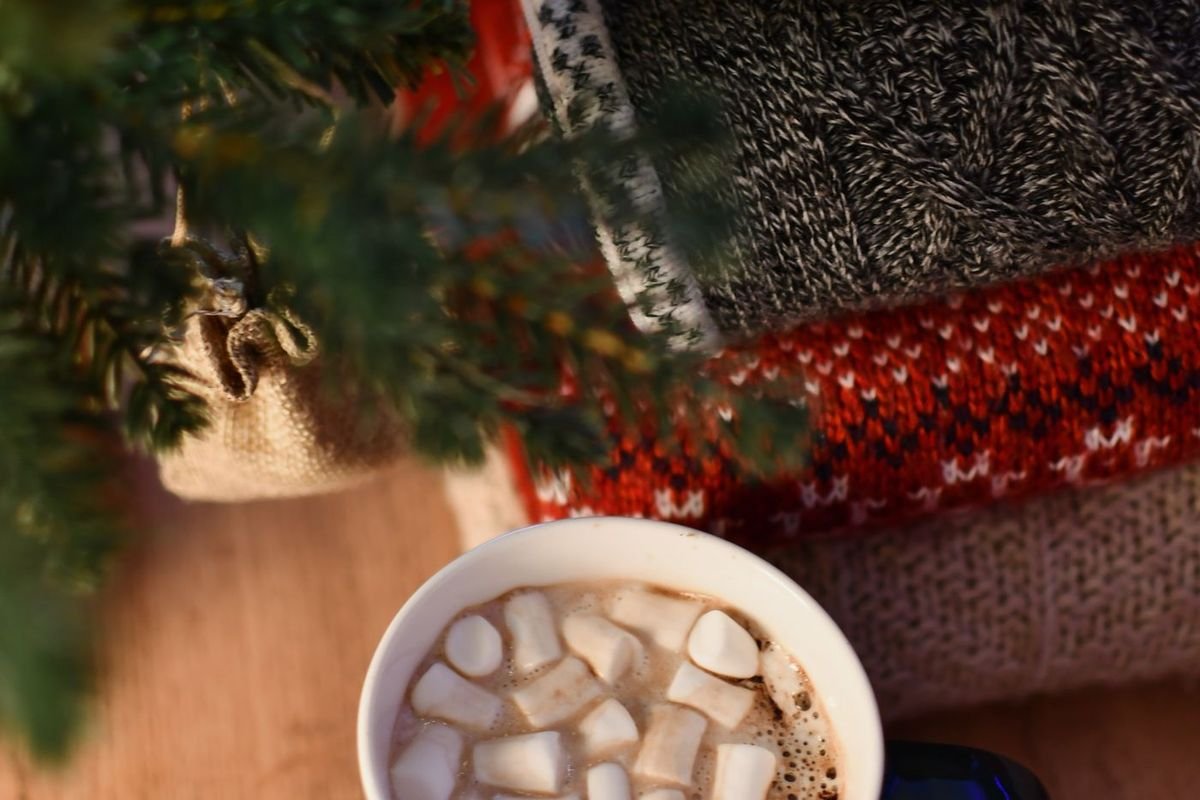 Mug of hot cocoa with marshmallows next to cozy knit sweaters