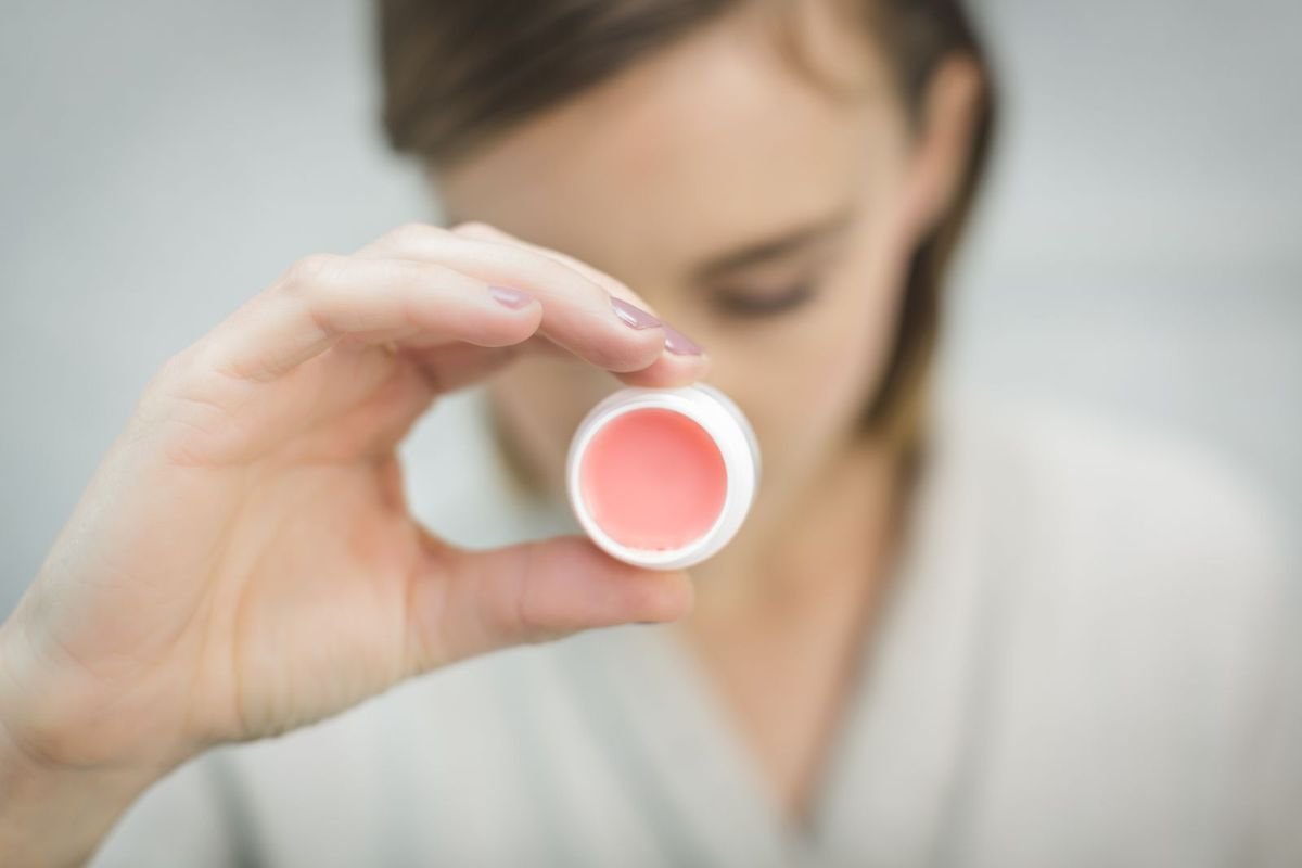 Hand holding a pink lip balm container (representative photo, not the exact product)