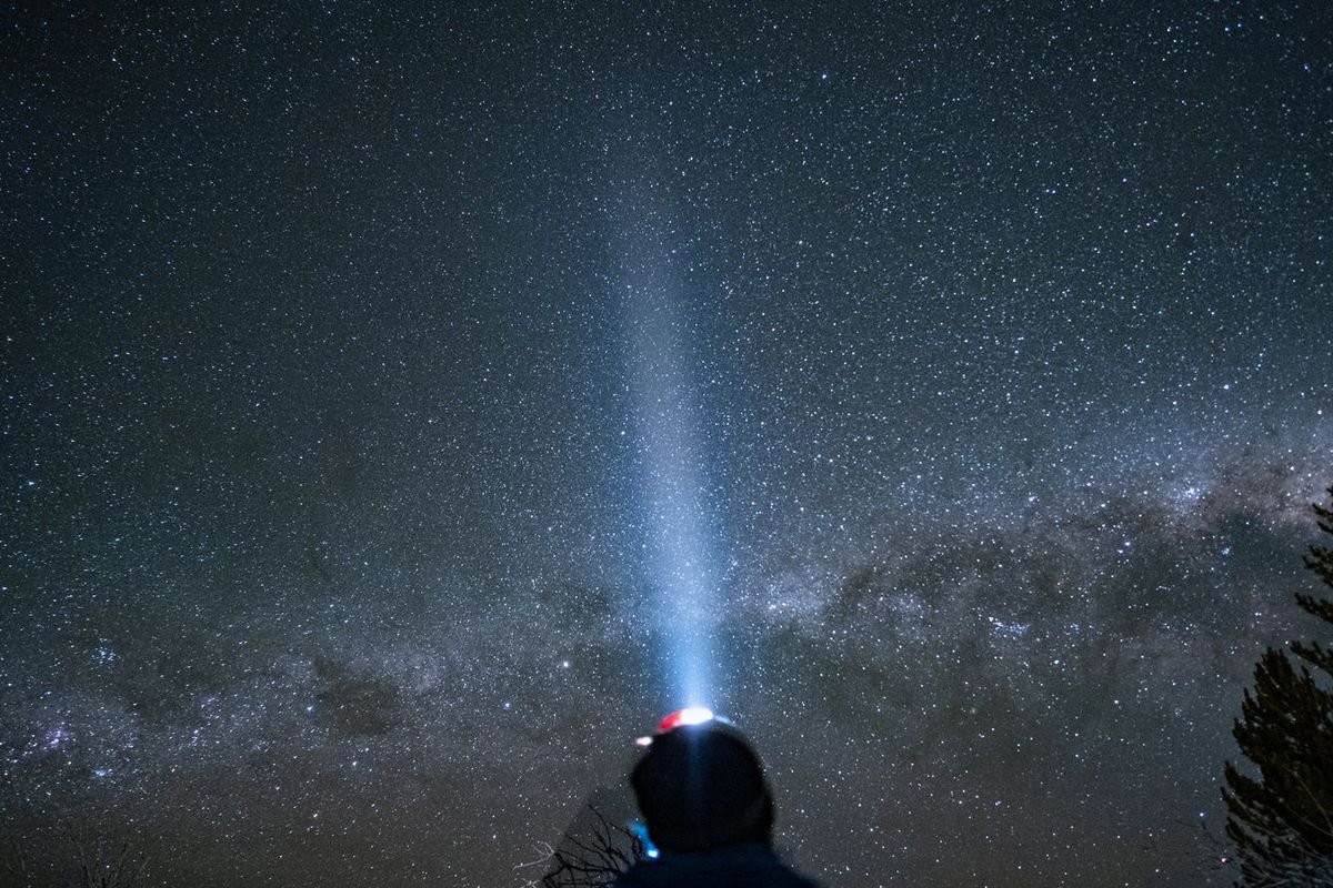 Person with a flashlight under a starry night sky (representative photo, not the exact product)