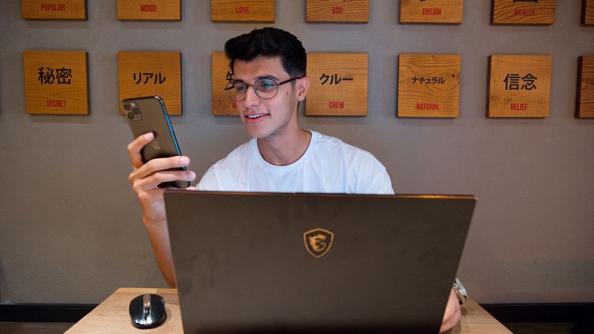 Smiling man holding a smartphone at his desk with a laptop and mouse
