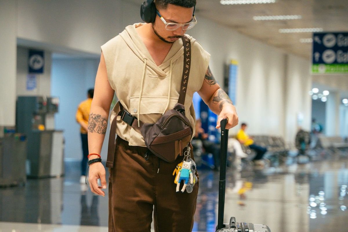 Young man with headphones and a suitcase walking through an airport terminal