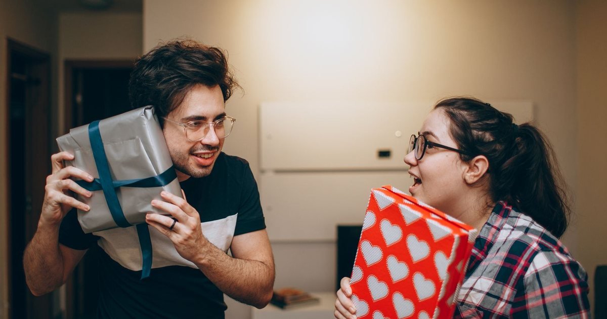 Two friends exchanging wrapped holiday gifts at home