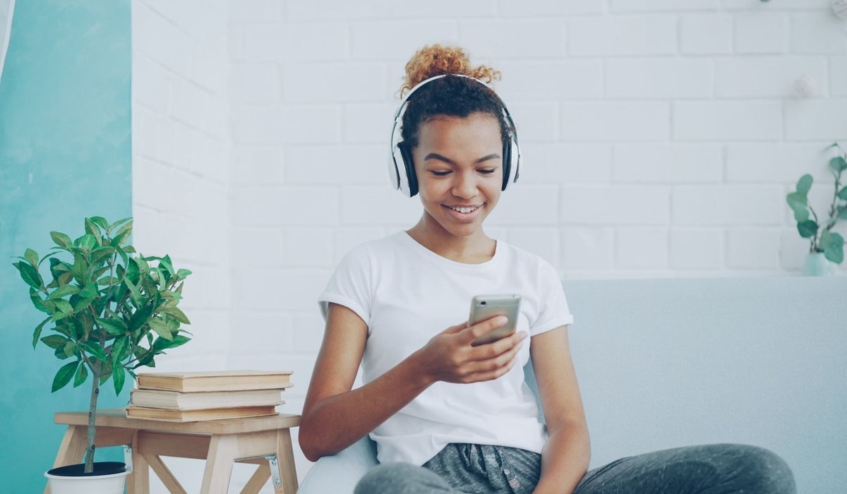 Smiling teen listening to music on headphones while texting