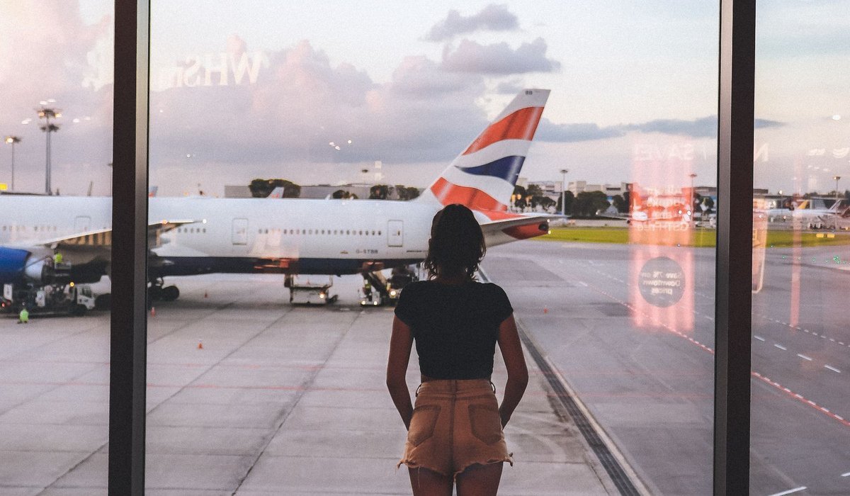 Traveler looking out a large airport window at a parked passenger jet