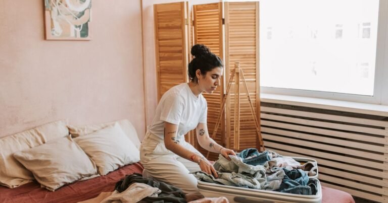Woman packing clothes into an open suitcase on her bed in a bright bedroom