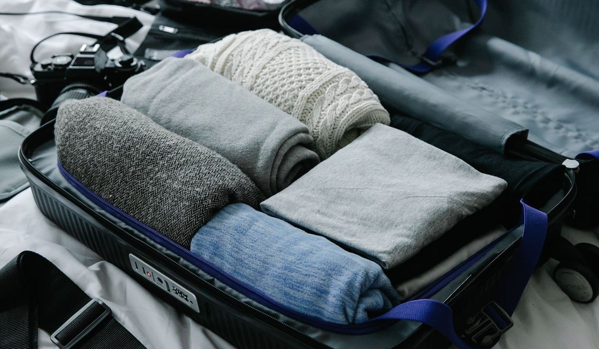 Open suitcase packed with neatly rolled sweaters and clothes on a bed