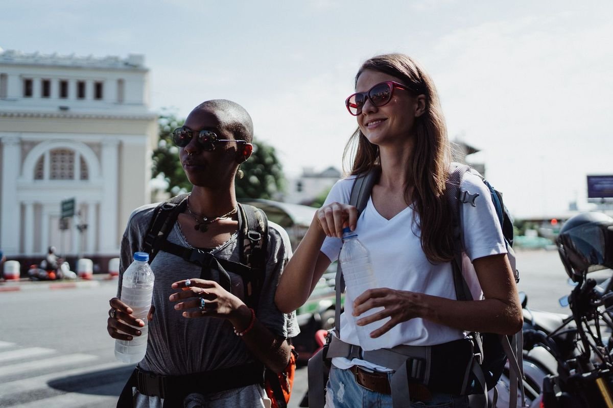 Two travelers with backpacks holding water bottles on a sunny street (representative photo, not the exact product)