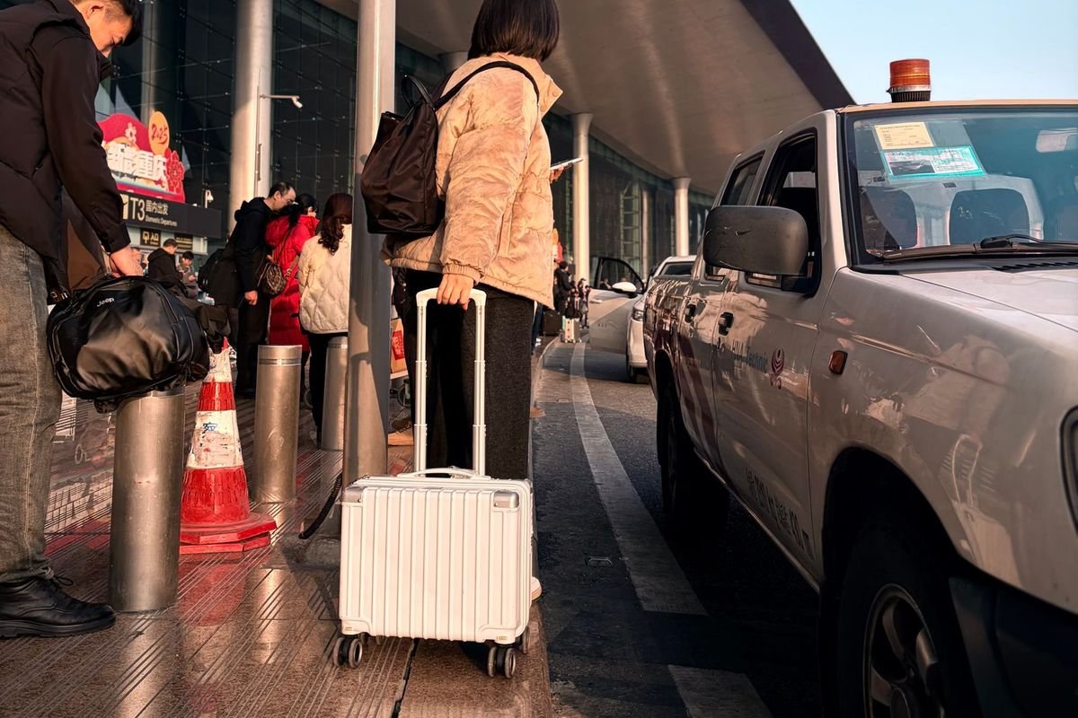 Traveler at an airport curb with a rolling suitcase (representative photo, not the exact product)