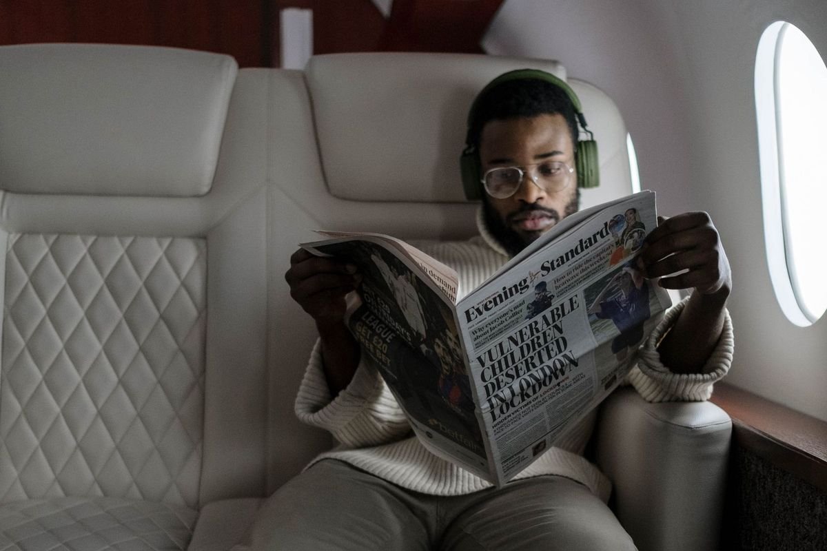 Man wearing over-ear headphones while reading a newspaper in an airplane cabin (representative photo, not the exact product)