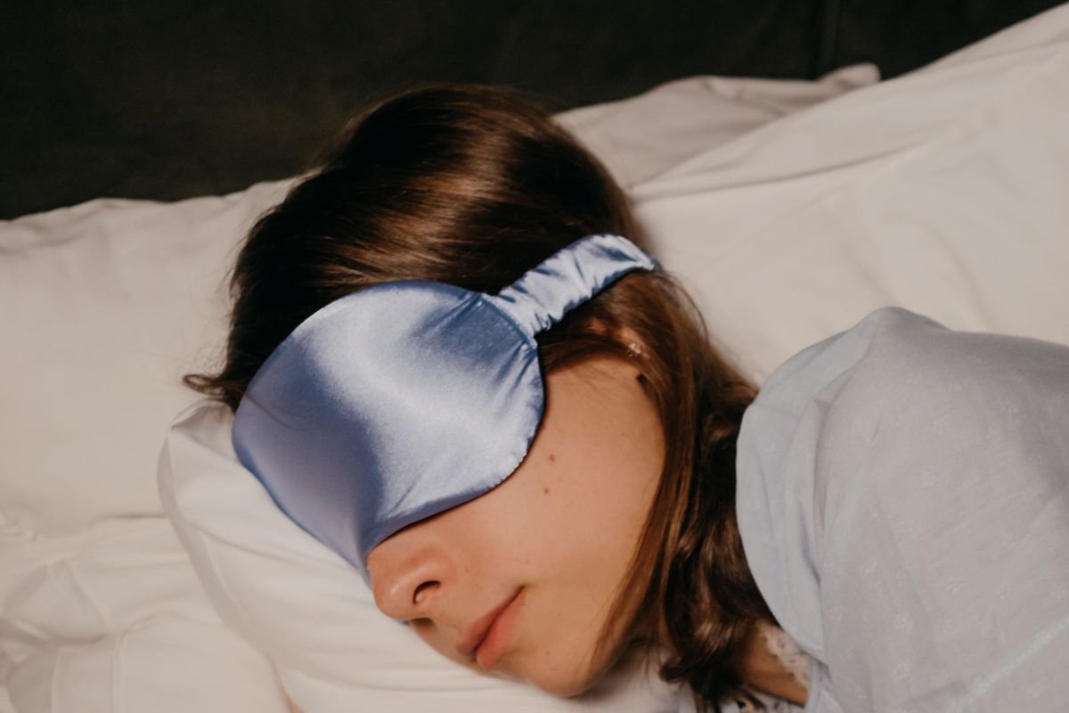 Woman sleeping peacefully in bed wearing a satin eye mask (representative photo, not the exact product)