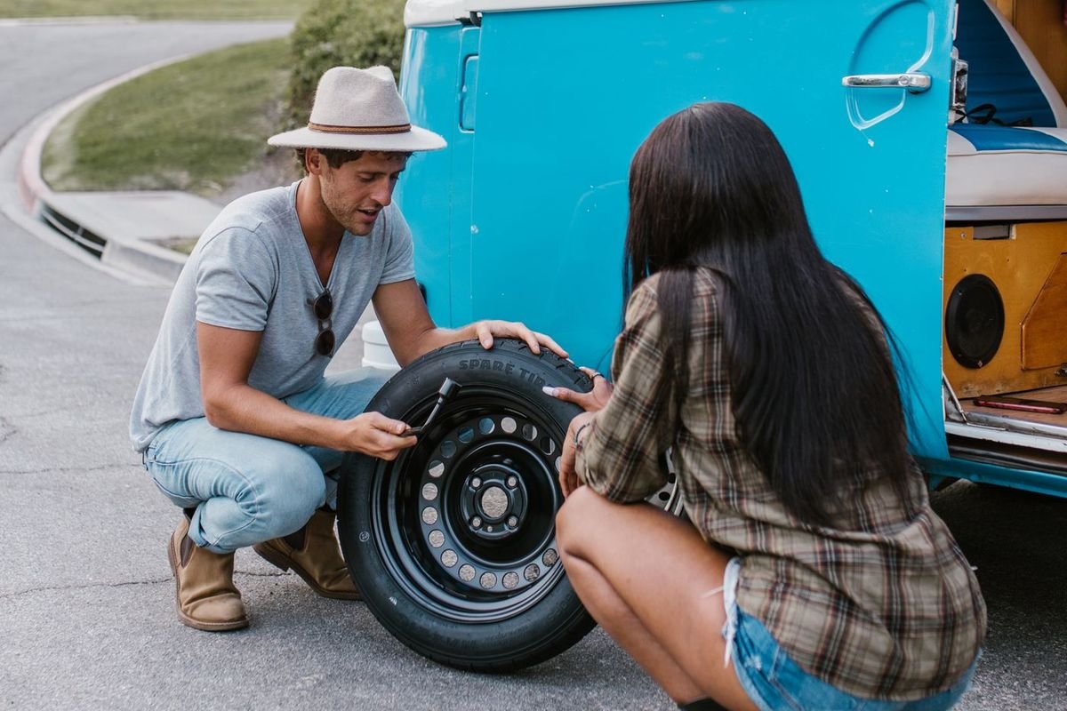 Couple changing a tire on a vintage blue camper van
