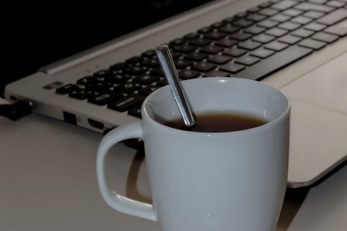 White coffee mug next to an open laptop (representative photo, not the exact product)
