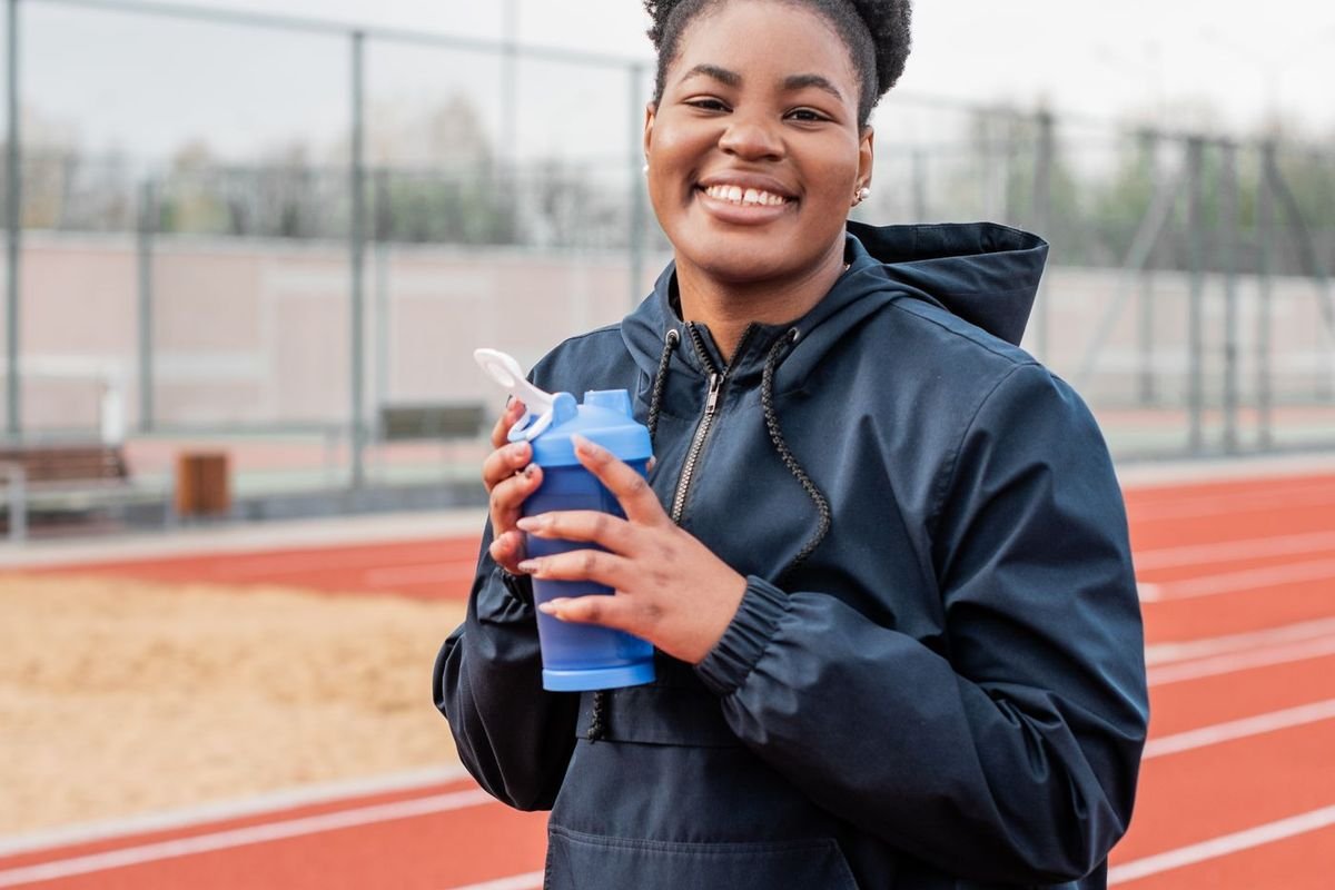 Smiling woman in a blue jacket holding a water bottle outdoors