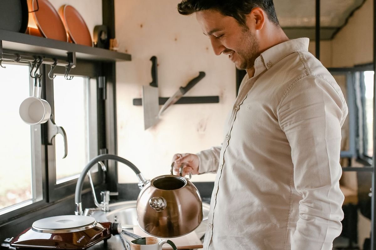 Man pouring hot water from a kettle into a mug in a stylish kitchen