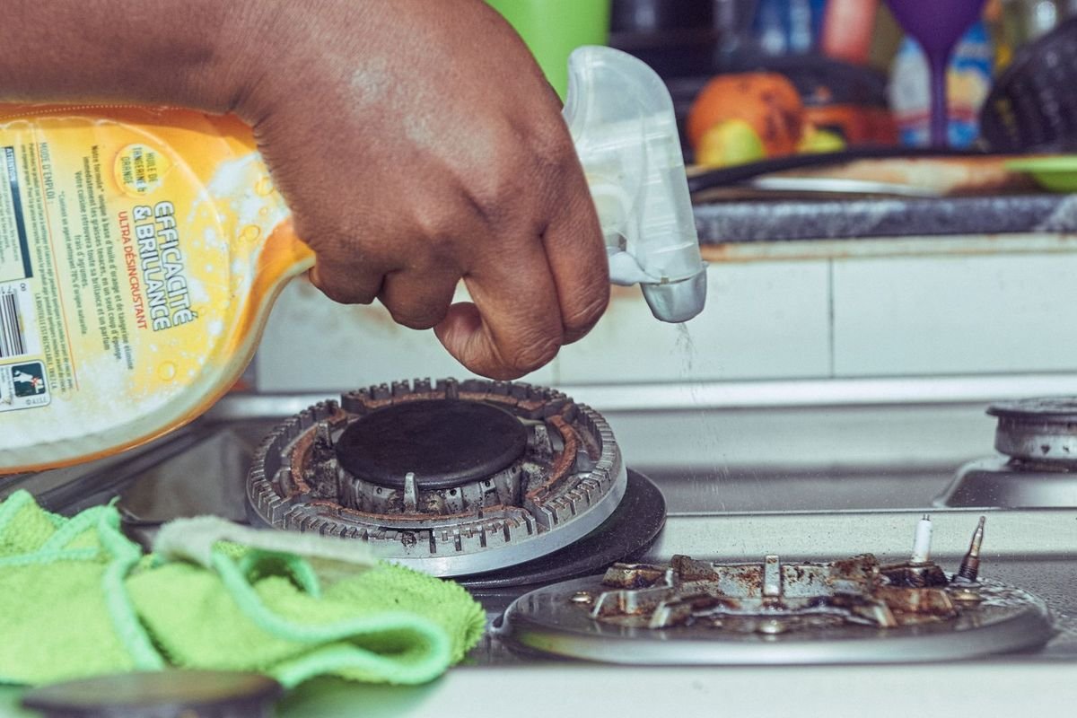 Hand cleaning a gas stovetop (representative photo, not the exact product)